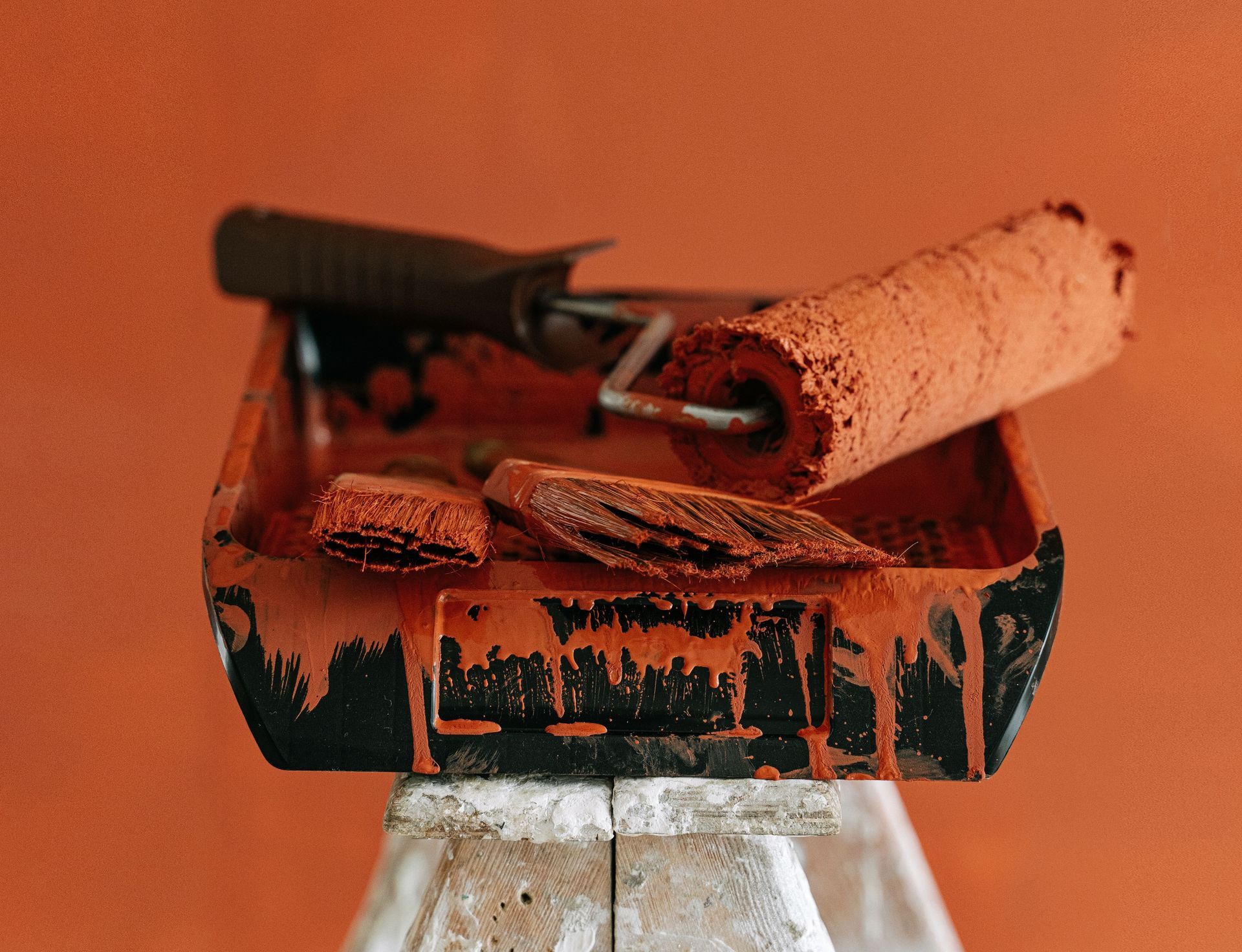 A stepladder holds paint tools for a vibrant orange home renovation project.