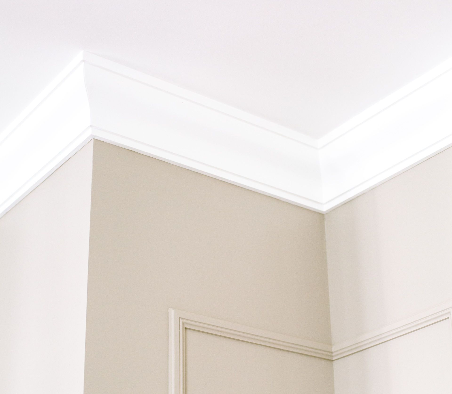 Close-up of intricate ceiling moulding and beige walls with minimalist design, showcasing home renovation details.
